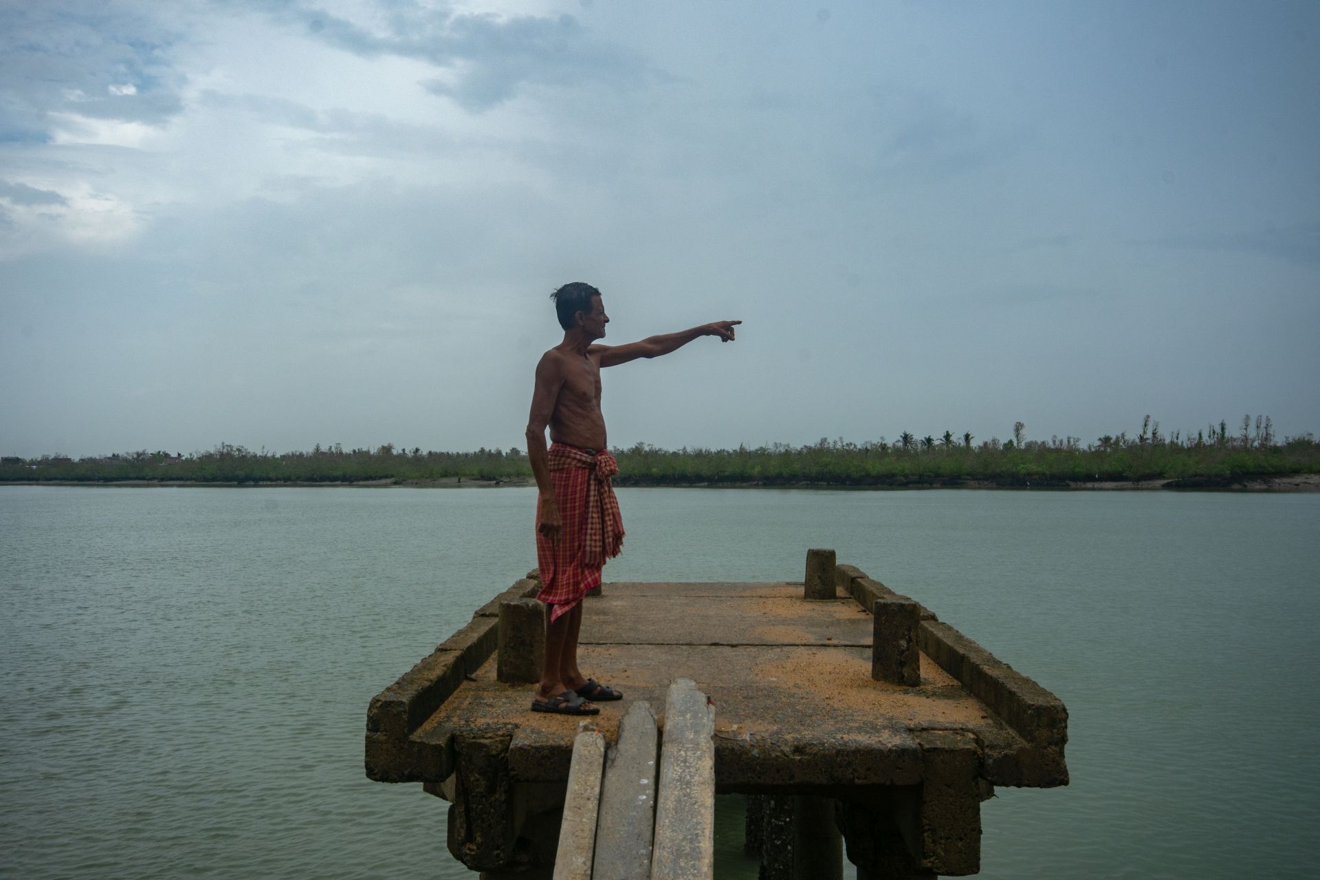 Gaur Hari Maity points at the Chaltamuniya Khal which has now turned into a river due to the rise in seawater in the recent past. (Image: WaterAid/ Subhrajit Sen)