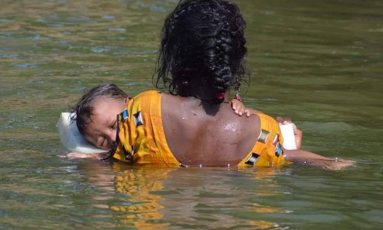 बाढ़ में बच्चे को सुरक्षित स्थान पर ले जाती महिला फोटो क्रेडिट माधव